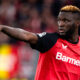 Victor Boniface con il braccio teso indica qualcosa ai compagni di squadra del Bayer Leverkusen durante una partita