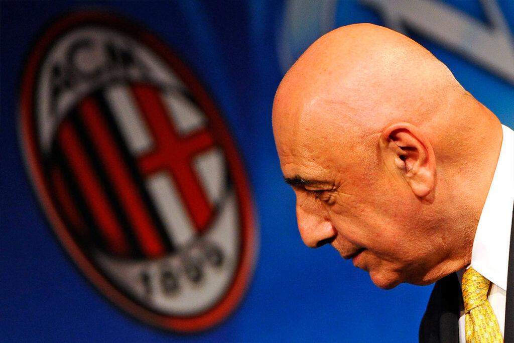 Adriano Galliani di profilo in primo piano con il logo del Milan sfocato alle spalle